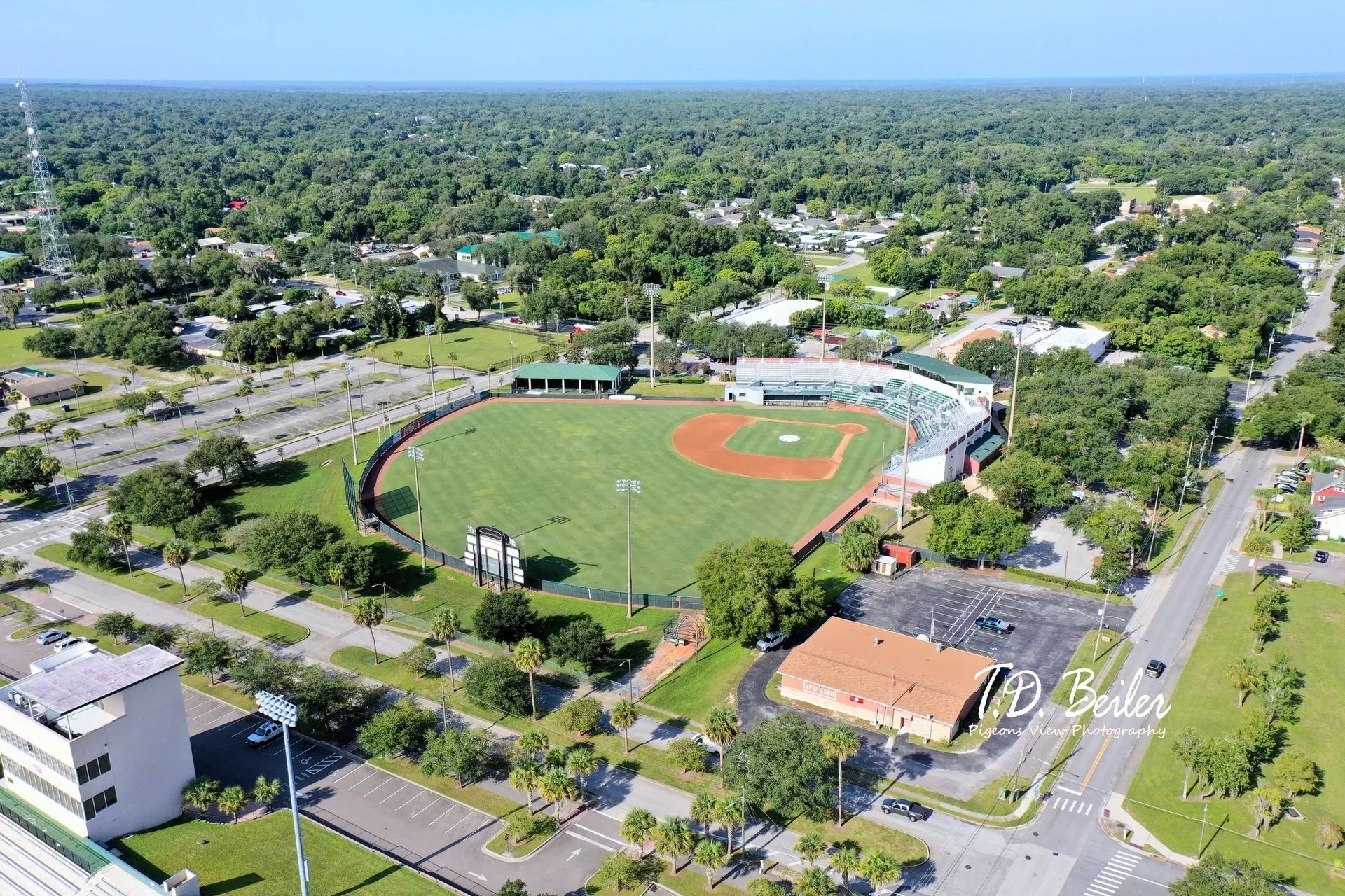 Baseball field amidst green trees and roads.