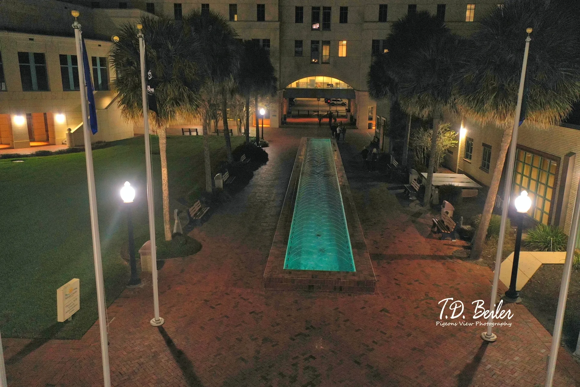 Long fountain glows in dimly lit courtyard.