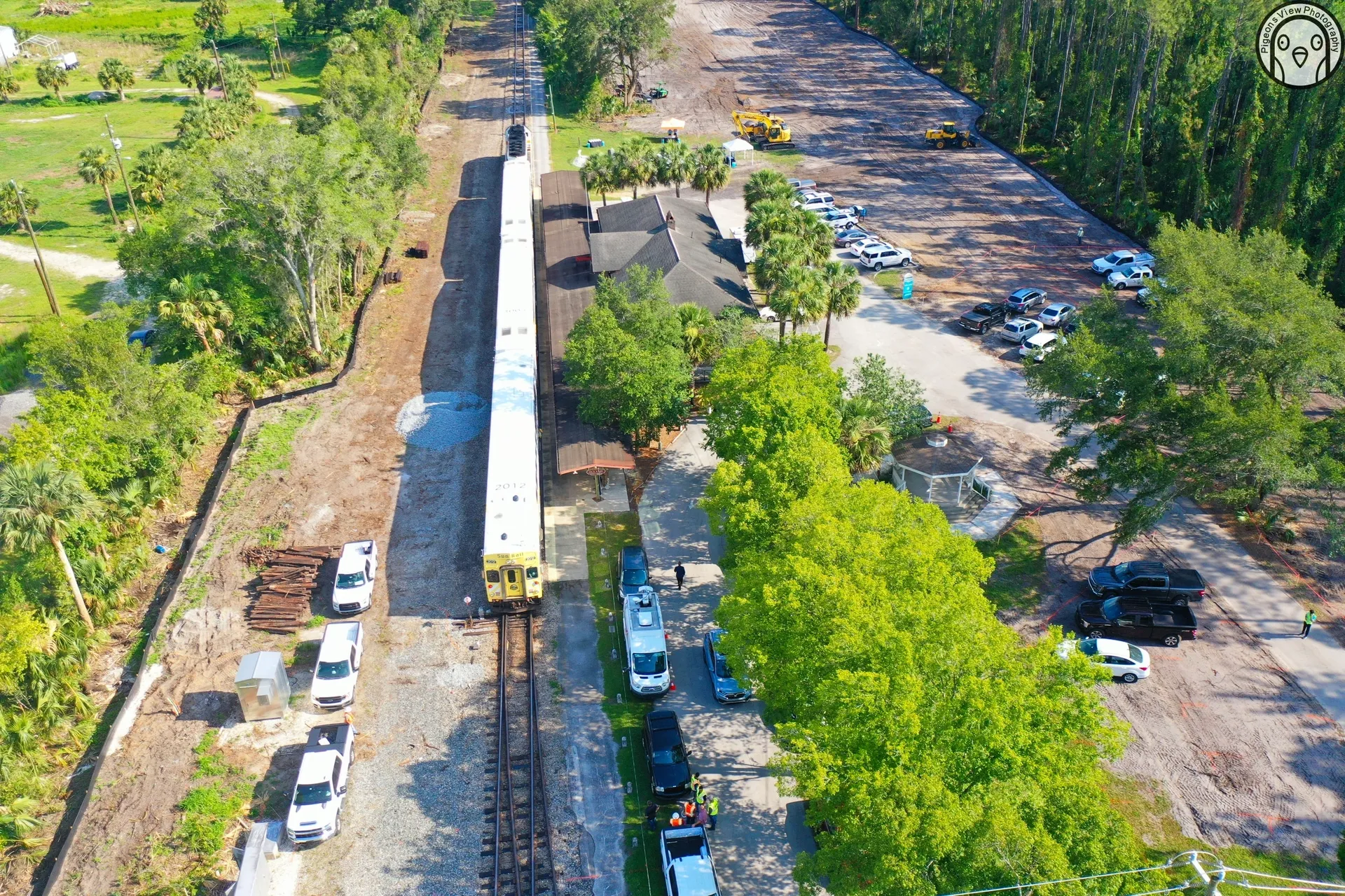 Train surrounded by greenery and vehicles.